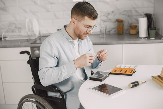 Man in wheelchair repairing electronics at home using tools, showcasing independence.
