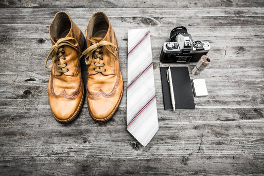 Flat lay of vintage camera, shoes, tie, and notebook on rustic wood surface.