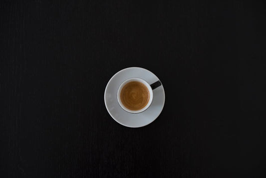 Flat lay of a white coffee cup with espresso on a black table, highlighting minimalist design.