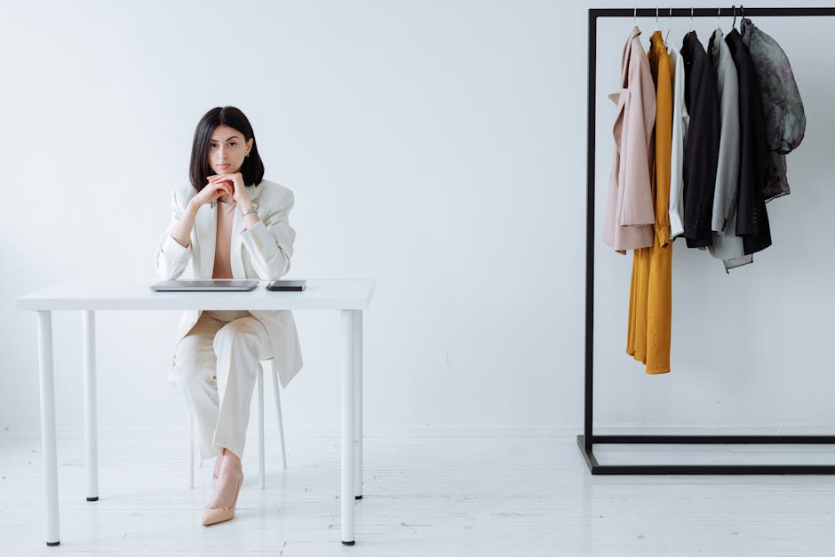 Modern businesswoman sitting at desk with clothing rack, embodying fashion and professionalism.